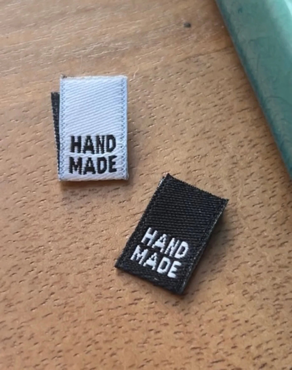 Close up of two  black and white Kati Cupcake mini 'HAND MADE' woven labels on a wooden surface