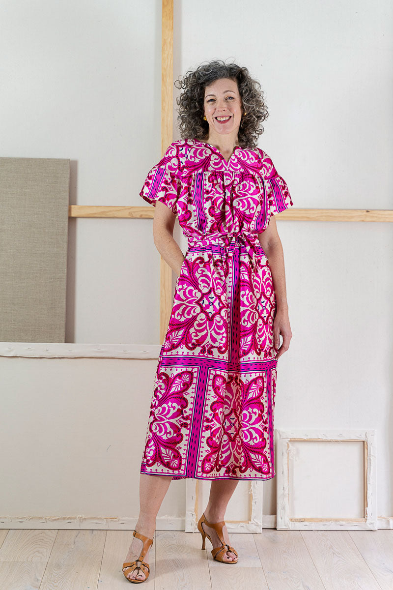Woman wearing a pink and white patterned Positano dress standing indoors.