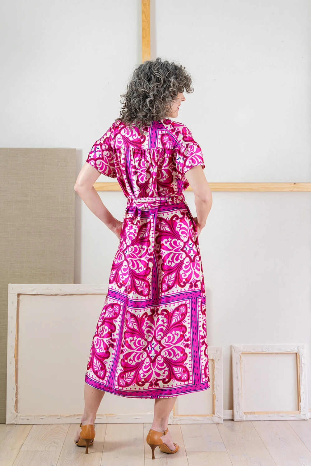 Rear view of woman wearing a pink and white patterned Positano dress standing in a minimal indoor setting.