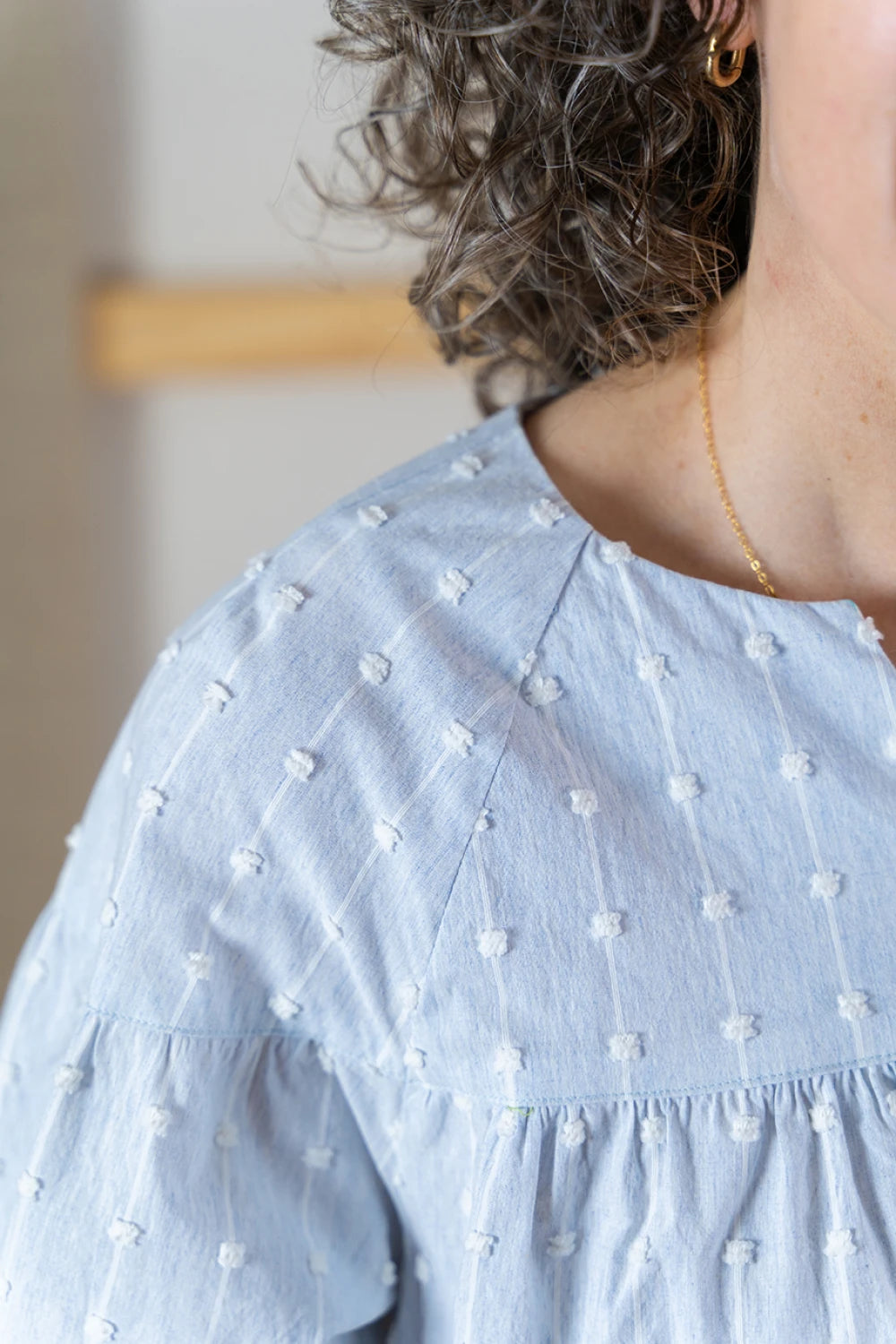 Close up of shoulder on a light blue Positano blouse with white patterns worn by a person.