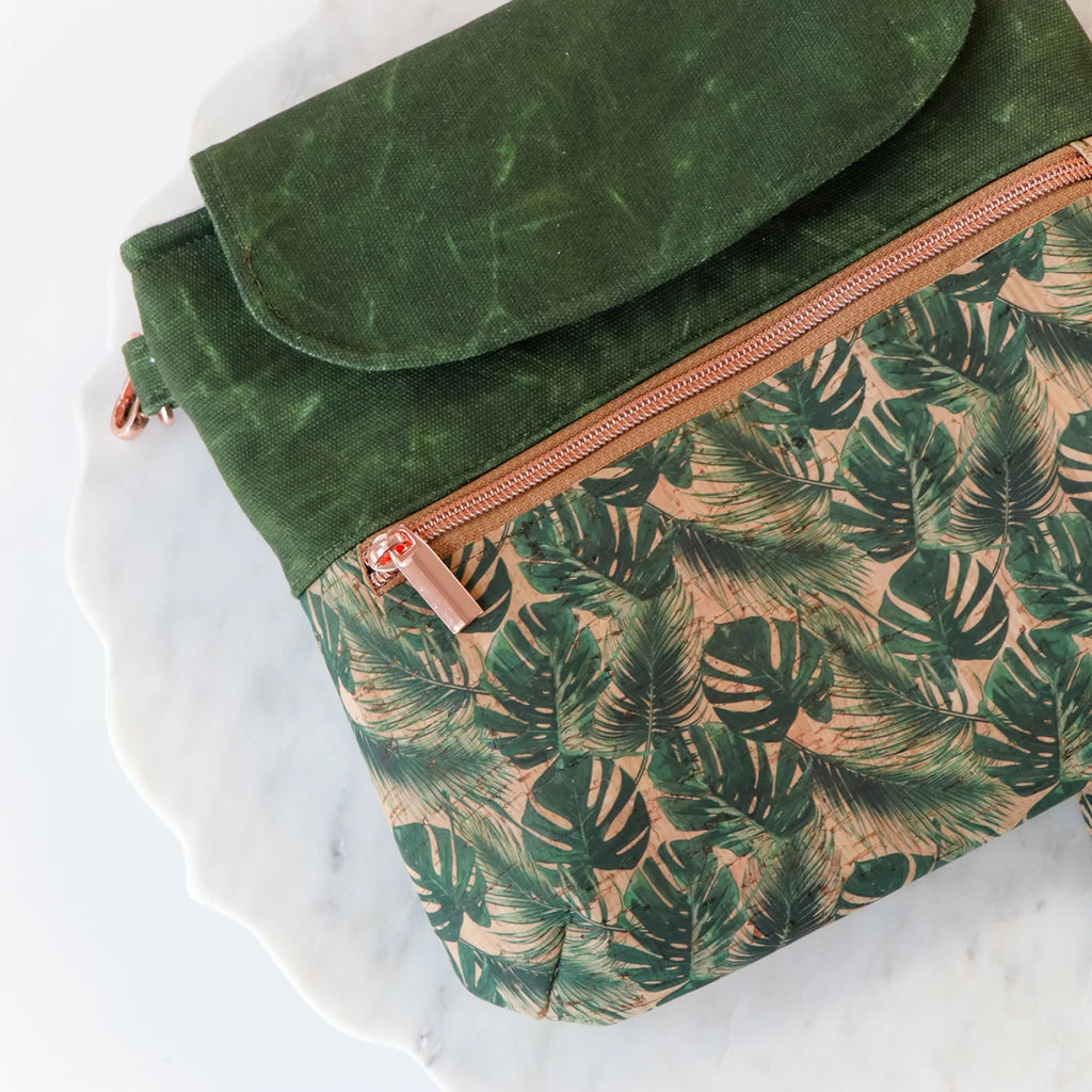 Green canvas and cork bag with a tropical leaf pattern on a white marble surface