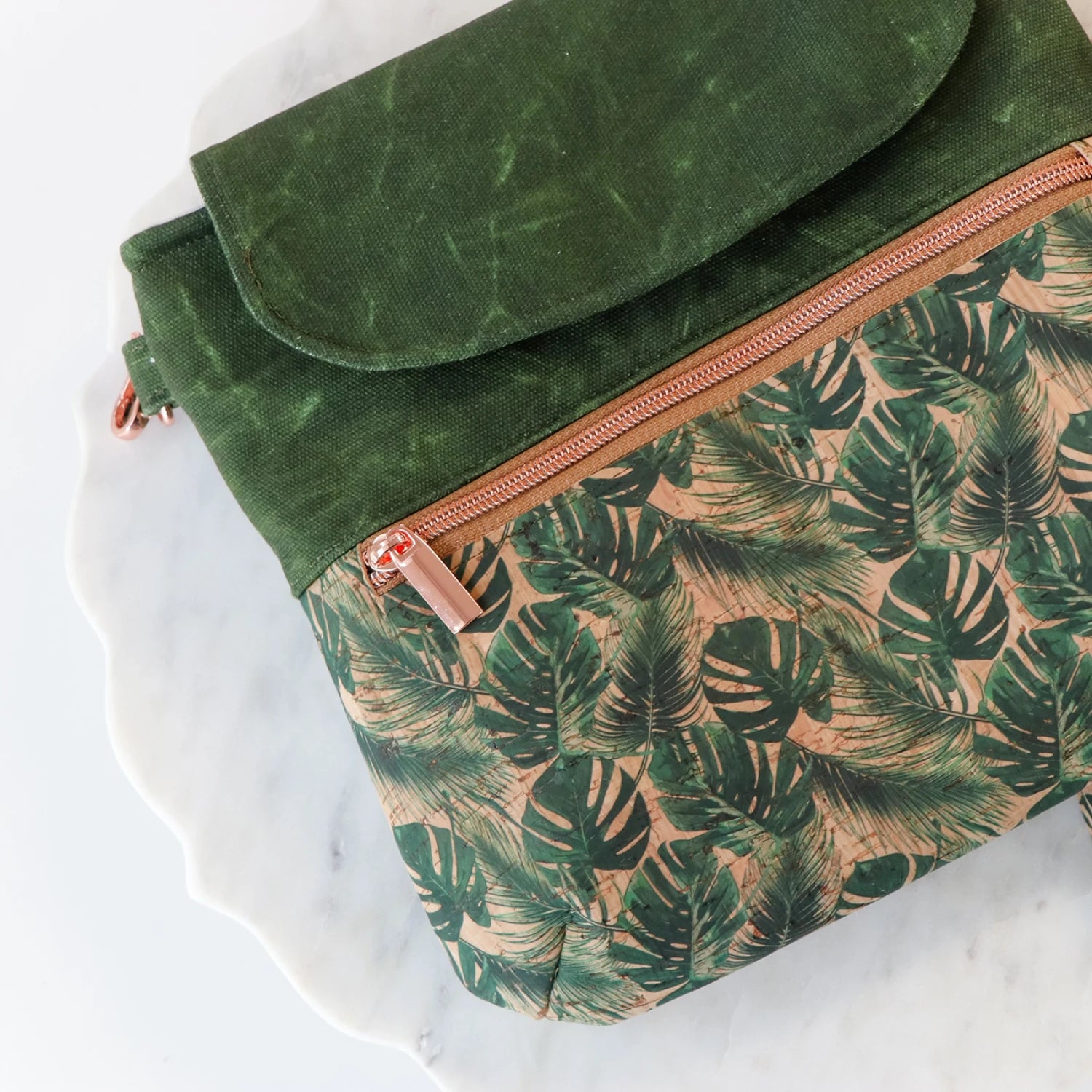 Green canvas and cork bag with a tropical leaf pattern on a white marble surface