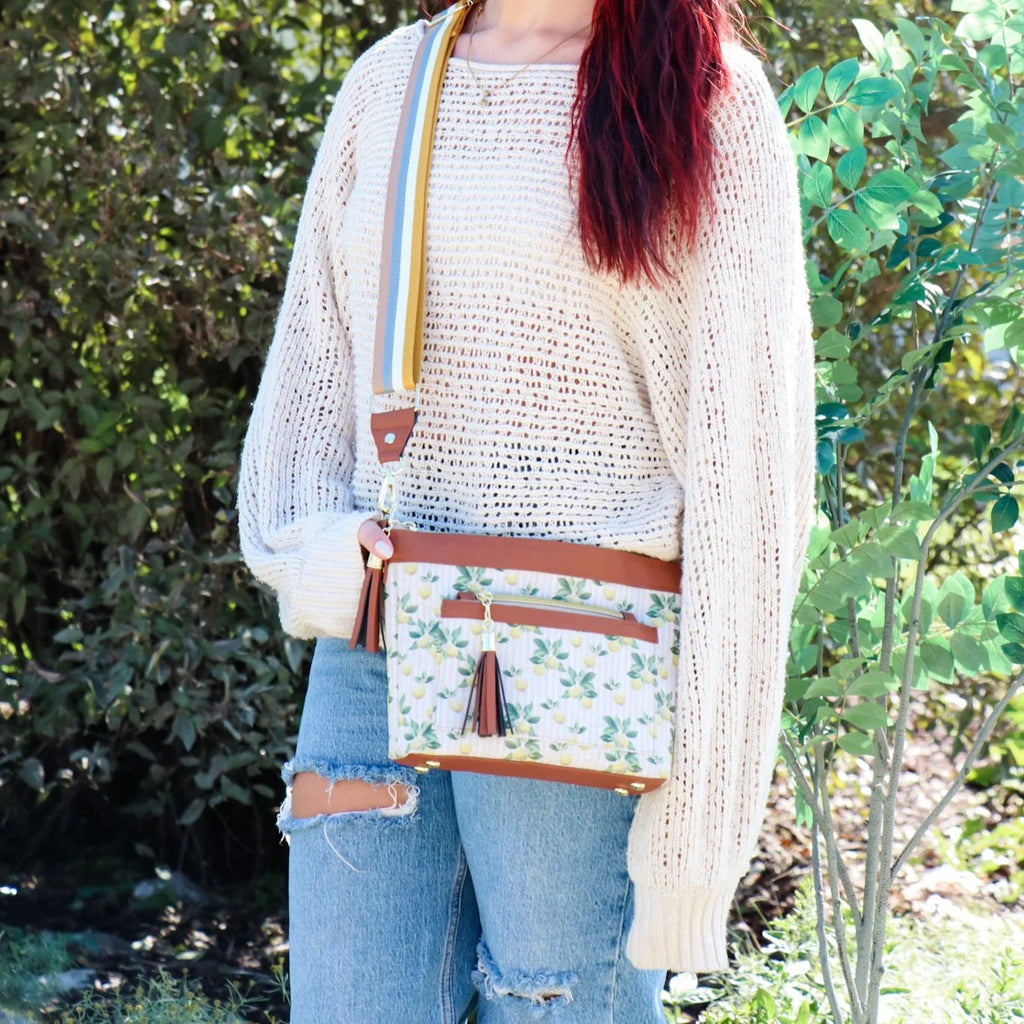 Person holding a floral crossbody bag outdoors with greenery in the background