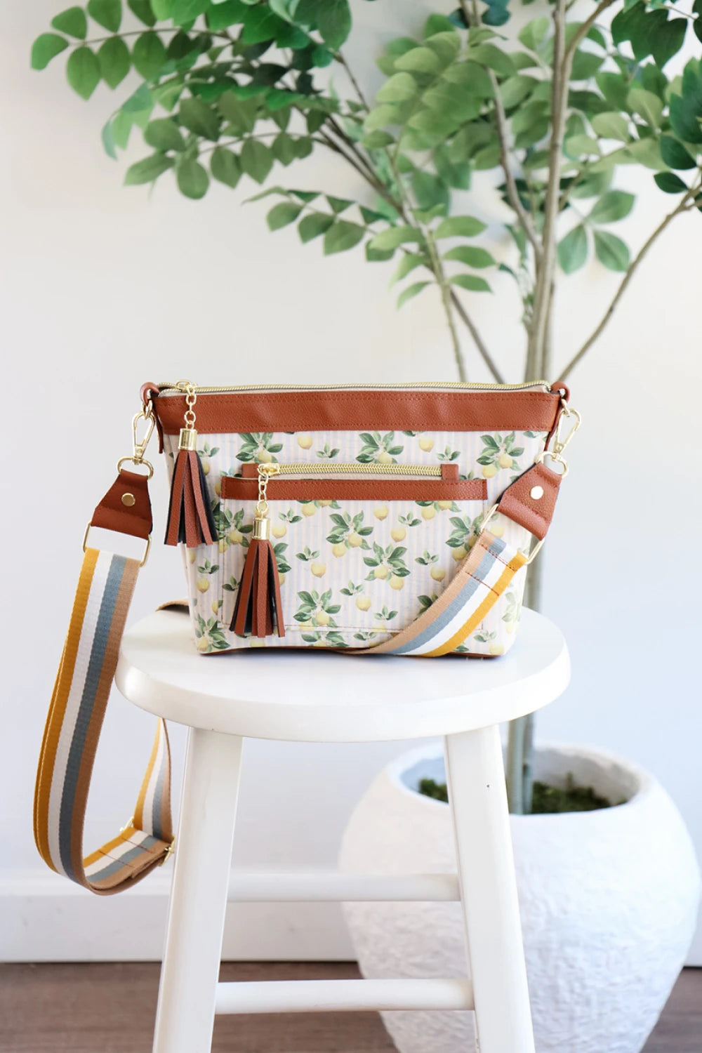 Floral patterned handbag with brown accents on a white stool against a white wall with plants.
