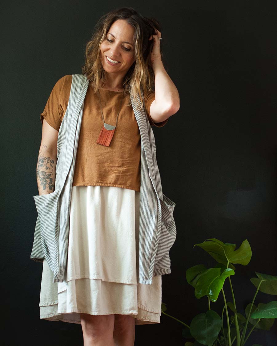 Woman wearing a layered outfit with a vest and short sleeve shirt over a skirt against a dark background